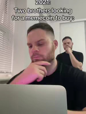 The image shows two young men in a room with blinds. The foreground shows a man looking down at what appears to be a laptop. The second man is in the background, leaning against the wall and resting his chin on his hand. Text overlayed on the image reads "2021: Two brothers looking for a memecoin to buy:"