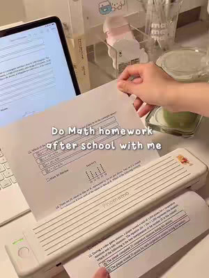 The image shows a desk setup with a computer screen, a white sheet with homework questions on it, and a hand holding the paper. The text overlay reads: "Do Math homework after school with me". The background includes stationery and a green drink.