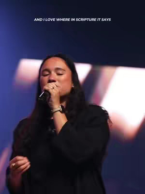 A woman singing into a microphone with a black top, the background has bright highlights and the text overlay on the top.
