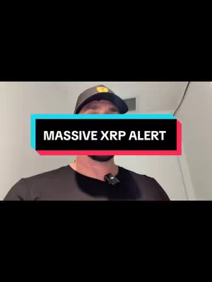 A man in a black t-shirt and a baseball cap is centered in a vertical video frame. The man is in front of a white wall, and the background is plain. A rectangular text overlay with the words "MASSIVE XRP ALERT" in white font is positioned in front of him, with a black background and red and teal borders. A microphone is clipped to his shirt.