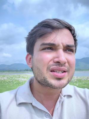 A selfie-style shot featuring a man looking slightly to the side with a concerned expression, set against a backdrop of a calm, cloudy sky, distant hills, and a body of water.