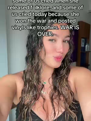 A selfie-style shot featuring a young woman with long, wavy hair. She has light skin and is wearing a black top. She's in a close-up smiling and making a kiss face. Text overlays the image. The background is a blurry interior.