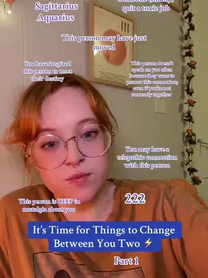 A young woman with auburn hair and round glasses looks directly at the camera. She's wearing a brown t-shirt. Text overlays are present with astrological signs and phrases predicting changes. The background includes a framed abstract artwork and a wall with decorative elements.