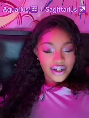 A close-up shot of a young woman with dark, curly hair wearing purple eyeshadow and lipstick. The background is a mix of black and pink hues. Text overlay at the top reads 'Aquarius + Sagittarius'.