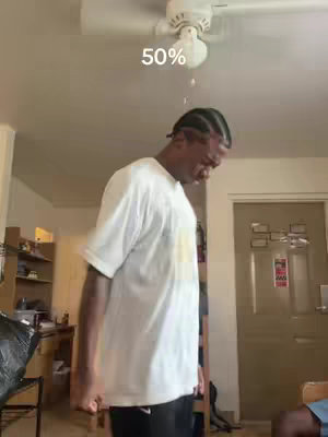 A man stands in what appears to be a living room, with text overlayed near the ceiling. The man is wearing a white t-shirt and his head is slightly tilted down. The ceiling has a ceiling fan in the center emitting water, possibly representing the content of the video.