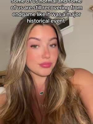 A selfie-style shot features a young woman with long, light-brown hair, soft lighting, and a subtle smile. She's wearing light makeup and a delicate necklace, suggesting a casual yet polished look. The background is out of focus and the framing is close-up.