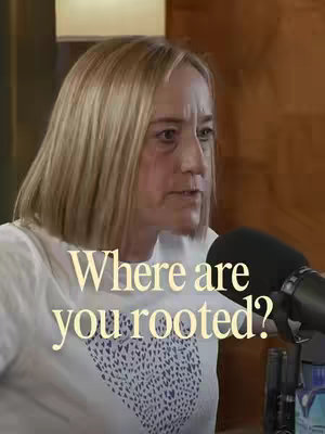 The cover image features a woman with blonde hair and a white top, looking slightly off-camera with a thoughtful expression. The text overlay reads 'Where are you rooted?' in a cream-colored font, superimposed over her torso. A dark microphone is visible on the right, suggesting a podcast or interview setting.