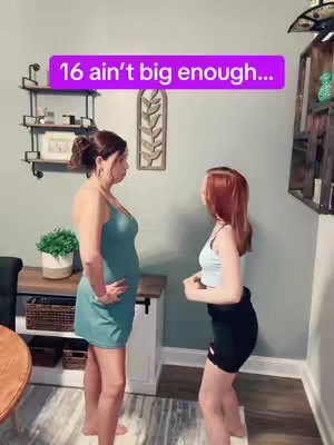Two women, presumably a mother and daughter, stand facing each other in a room. The mother is on the left, wearing a short, teal dress. The daughter is on the right, wearing a light blue top and dark shorts. A text overlay in a purple rectangle reads "16 ain't big enough...". The background includes a wall, decor, a table and lighting.