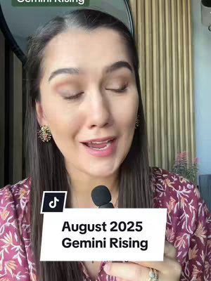 A woman with a light complexion speaks directly to the camera, framed from the chest up. She has brown hair and is wearing a floral patterned shirt. She has makeup on her eyes. A white rectangular sticker with black text that says, "August 2025 Gemini Rising" is placed in the center of the frame. In the upper left corner is text that says Gemini Rising.