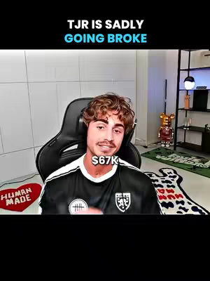 The image features a man with curly brown hair and a goatee, sitting in a black gaming chair. Above him is a black banner with the text "TJR IS SADLY GOING BROKE" in white and blue. Below his face is a white tag that says '$67K'. He is wearing a black and white soccer jersey-like shirt. The background shows a modern room setup with decorative items like a heart-shaped rug and a decorative bear.