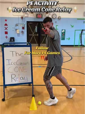 A man in a grey shirt and patterned shorts points towards the viewer; behind him is a whiteboard with handwritten text and a yellow traffic cone, tennis ball on the floor. The background is a gymnasium with a basketball court. Text overlays include 'PE ACTIVITY' and 'Ice Cream Cone Relay'.