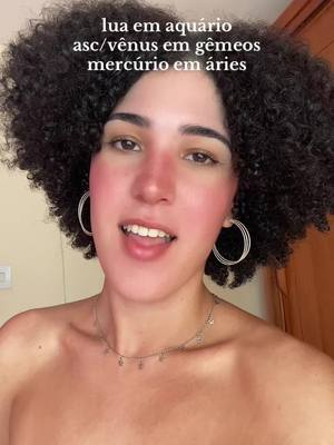 A selfie-style shot featuring a woman with curly dark hair and fair skin. She's smiling with her mouth open, revealing her teeth. She has light makeup with the focus on her blush and pink tones. She's wearing hoop earrings and a delicate necklace. The background is blurred, and text appears at the top.