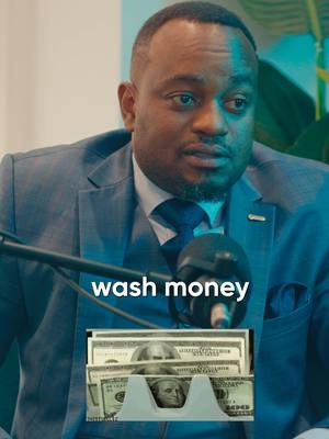 A man in a suit is seated, with a microphone in hand and a money holder with dollar bills in it. The words 'wash money' are overlaid on the picture.