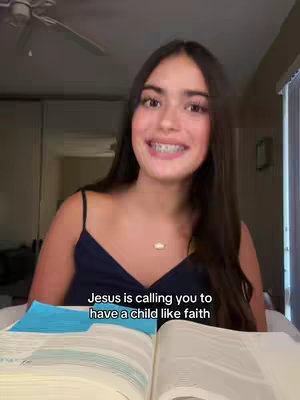 A young woman with long brown hair is smiling at the camera while sitting near an open Bible. Text overlayed on the image reads, "Jesus is calling you to have a child like faith"