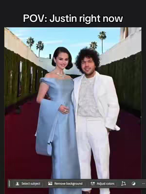The image shows a red carpet scene with two celebrities standing side-by-side: Selena Gomez in a light blue gown and Benny Blanco in a white suit. The overlay text at the top reads "POV: Justin right now". The bottom shows software tool icons.