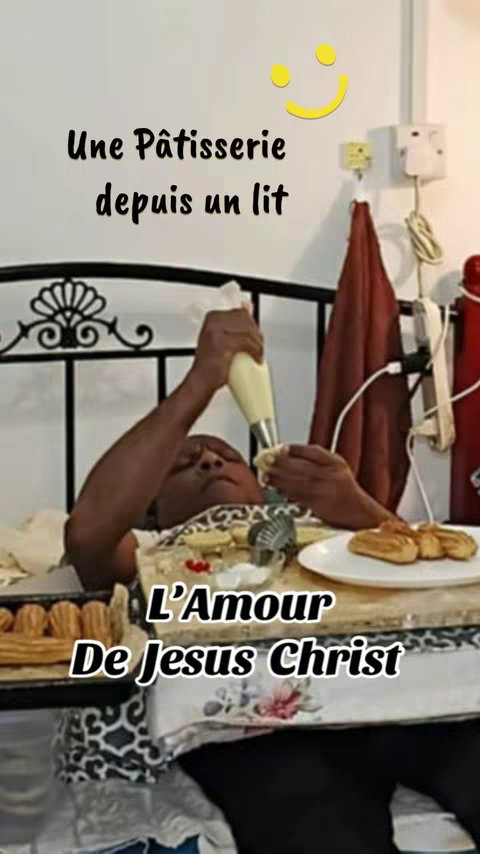 The cover image shows a man in bed, piping cream onto a pastry. Text overlays read "Une Pâtisserie depuis un lit" and "L'Amour De Jesus Christ". A yellow smiley face is placed above. Various baking supplies are visible.