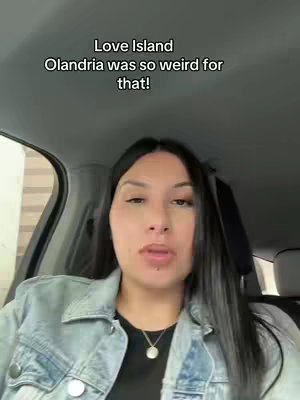 A woman is filmed from the chest up, in a car, facing forward, with text overlayed and a background.