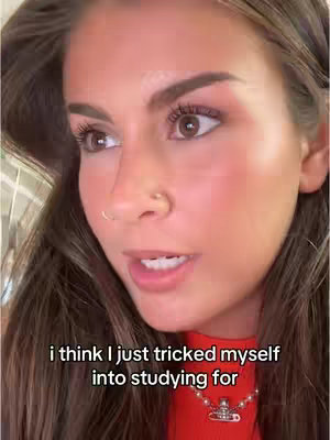 A close-up shot of a young woman's face, with her gazing slightly to the side. She has dark eyebrows and a small nose ring. The video appears to be taken indoors, with soft lighting. The woman is wearing a red top, necklace. The background is slightly out of focus.