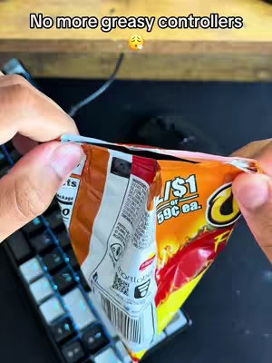 A close-up shot shows a person's hands holding an opened bag of Cheetos. The bag is orange and filled with the chips. The person's hands are the focal point, with a keyboard and a mouse blurred in the background, suggesting a gaming setup. Above, text adds to the image.