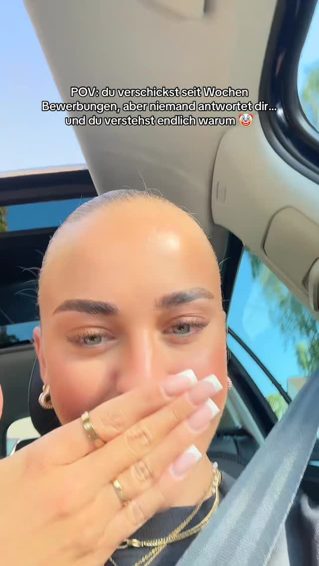 The image is a selfie-style shot of a light-skinned woman inside a car. She's covering her mouth with her right hand. Her nails are painted with a French manicure. The text is overlaid on the image reflecting the emotional state, and the angle is a close-up from the chest up, inside the car.