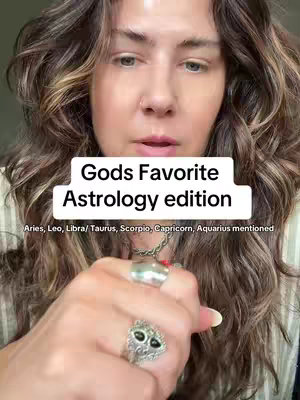 The cover image features a woman with long, wavy brown hair looking towards the camera. A white box overlay centered on the image reads "Gods Favorite Astrology edition" in a bold, black font. Below this, smaller white text lists various astrological signs mentioned. The woman has fair skin, and her hand is visible at the bottom, adorned with rings.