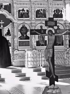A grayscale image captures the interior of a church or religious building. The central focus is a large, dark crucifix with the figure of Jesus Christ. Behind, the ornate interior is visible. Walls are decorated with religious iconography, and there are steps leading up to what seems to be the altar. The lighting is natural, casting shadows and highlighting details.