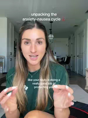 A woman is addressing the camera, positioned in front of a bright, clean interior, likely a home, with white cabinets and a pendant lamp. The focus is on the woman, who is actively speaking, with text overlays suggesting a conversation about anxiety and nausea. The woman is wearing a green shirt, and her hands are up.