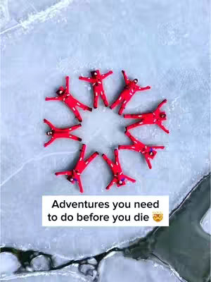 The image offers a top-down view of multiple figures arranged in a circular formation on a light blue surface, possibly ice or snow. Each figure is dressed in a bright red outfit, creating a strong contrast with the pale background. At the bottom of the image is a text overlay.