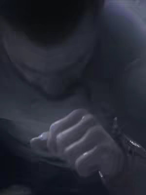 A dimly lit image featuring a close-up view of a hand, possibly male, clenching in a fist. The focus is on the hand, with the background details blurred out. The skin appears pale, and the lighting suggests a shadow or dark environment.