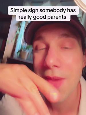 A man in a dark cap and a white shirt is captured in a close-up selfie. The man is gazing with his eyes closed, and a visible hand is situated in the frame's lower half.