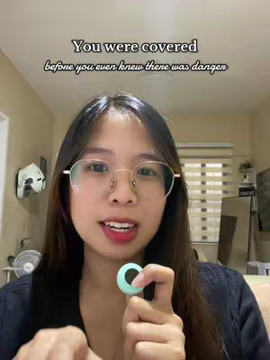 A woman with long dark hair and glasses looks at the camera while holding a teal object. Text overlay in a cursive font says 'You were covered before you even knew there was danger'