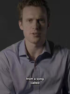 A man with short brown hair and a light blue button-down shirt speaks directly into the camera with a serious expression. Text on a black bar appears at the bottom, reading 'from a song called'.