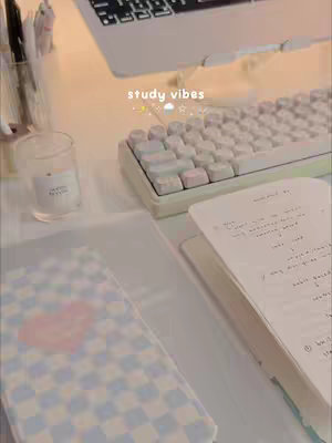 The cover image shows a well-lit, aesthetic desk setup. A white keyboard and a laptop are positioned behind a notebook with handwritten notes. In the foreground, there is a notebook, a candle in a clear glass, and a pen holder.