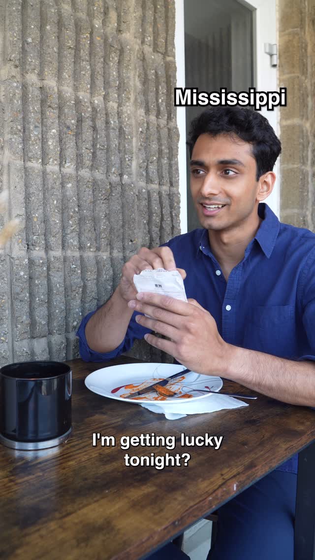 A man is seated at a wooden table with a black mug and a plate with food remnants in front of him. The background includes a textured concrete wall and part of a window. Text overlays the image.