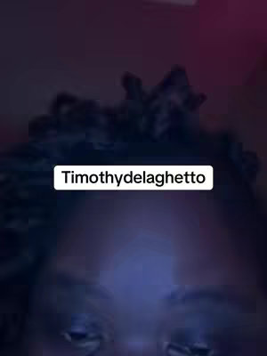 A selfie-style shot featuring the upper portion of a person's face against a dark background. The person's hair is dark and textured. A white rectangular overlay with the text 'Timothydelaghetto' is positioned at the top of the frame.