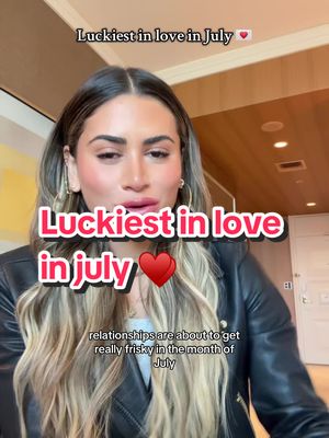 The cover image features a woman centered in the frame, looking towards the camera with a direct gaze. Overlaid on the image are several text elements in different text box shapes and sizes, the most prominent being "Luckiest in love" with a pink background and white text. A heart emoji is also prominently placed next to the main title. Below that, smaller text provides additional context. The woman is wearing a black leather jacket and has long, light-brown hair. The background appears to be a simple room with wooden paneling.