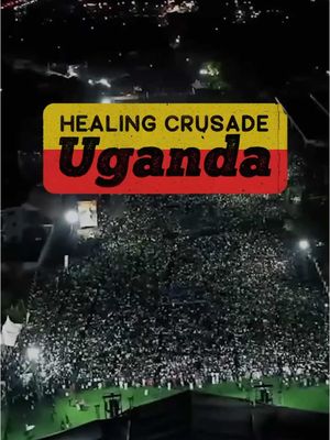 An aerial view of a nighttime outdoor gathering. A large crowd of people is illuminated from an elevated position, likely a stage or platform, with a large illuminated sign in the center that says "Healing Crusade Uganda". There is a dark background with city lights visible in the distance.