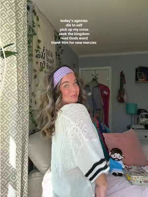 The cover image shows a woman in a room, seen from the waist up. She has long wavy hair and is wearing a light purple headband and a semi-sheer off-white knit cardigan. The background includes a window with white curtains, and a glimpse of a room with clothes hanging on a rack is visible. Text overlays the image on the upper-left side. In the foreground, the woman is turned with her back a bit to the camera and smiling. Colors are muted and natural, with greens from the plants and warm lighting suggesting a comfortable, indoor setting.