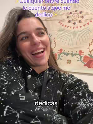 A woman with long brown hair is smiling widely at the camera and wearing a black hoodie. Above her, text is overlaid, while in the background, there's a tapestry with a circular design and floral patterns. Below her, at a lower part of the screen, a line of text is present.