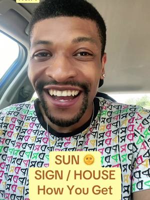 A selfie-style shot of a Black man smiling broadly and seated inside a car. He wears a vibrant, patterned shirt, and a text overlay appears in a yellow box, displaying text related to astrology. The background shows a car's interior.