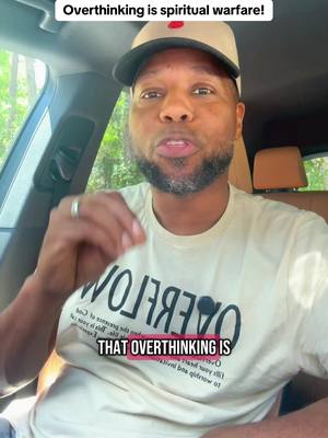 A middle-aged Black man with a trimmed beard wearing a baseball cap and a t-shirt is sitting in a car, speaking towards the camera. The background shows a glimpse of nature through the car window.