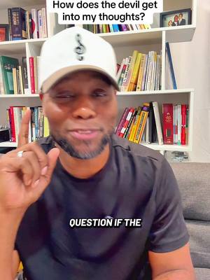 A man in a white cap and black shirt, with text overlayed at the top and bottom. He is in front of a bookshelf. The background is blurred out.
