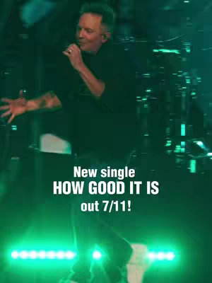 The image captures a live performance scene with a man performing on stage. He is holding a microphone and singing while wearing a dark outfit. The background is filled with musical equipment, and the stage is illuminated with dramatic green lighting. Overlayed text provides information about the single's release.