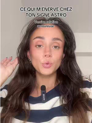 A young woman with long brown hair and light makeup looks directly at the camera and makes a kissing face. The background is a light-colored wall. Text overlays appear at the top of the screen: "CE QUI M'ÉNERVE CHEZ TON SIGNE ASTRO" and "Version relation amoureuse". A microphone is clipped to her shirt.