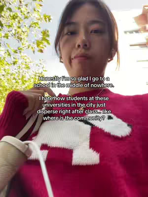 A selfie-style shot features a young woman in front of a slightly blurred outdoor background. She is wearing a red sweater has white dog-like graphic in the center. Her face is turned slightly towards the right, with a somewhat neutral expression. Text is overlaid on the image addressing her thoughts on community. The overall composition is natural and casual.