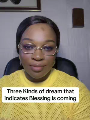 A woman with dark hair and glasses looks at the camera in a close-up shot. She is wearing a yellow sweater. White text at the bottom of the image reads, "Three Kinds of dream that indicates Blessing is coming". The background is a room with a framed picture and a light-colored wall.