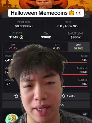 A cover image featuring a young Asian man in a selfie-style video, positioned in front of a screen displaying cryptocurrency market data. The image has a dark background, and the man is the focus, with the cryptocurrency information behind him. A banner at the top reads 'Halloween Memecoins🎃 👀'. The man has short black hair, and he directly addresses the camera.