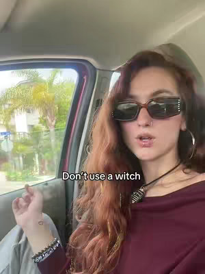 A woman with long auburn hair, wearing sunglasses, is seated inside a car with a palm tree visible through the window. Text overlayed on the image reads, "Don't use a witch."