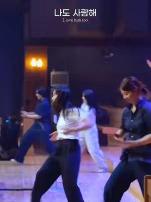 A group of women are dancing on a stage. The stage is lit with warm lighting. Text in Korean and English is displayed at the top of the image.
