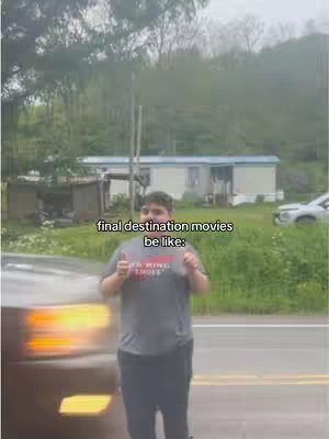 The cover image features a man giving a thumbs-up in front of a road and a house. The man is wearing a gray t-shirt and black pants. Behind him is a trailer or small house, trees, and a cloudy sky. The text overlay says "final destination movies be like:"